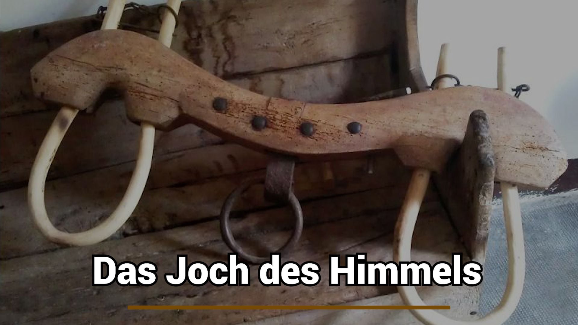 5. Das Joch des Himmels. An old wooden yoke with metal rings and white straps, displayed against a backdrop of aged wooden planks. German text overlay reads "Das Joch des Himmels" translating to "The Yoke of the Heavens." Opens a video in a new window.