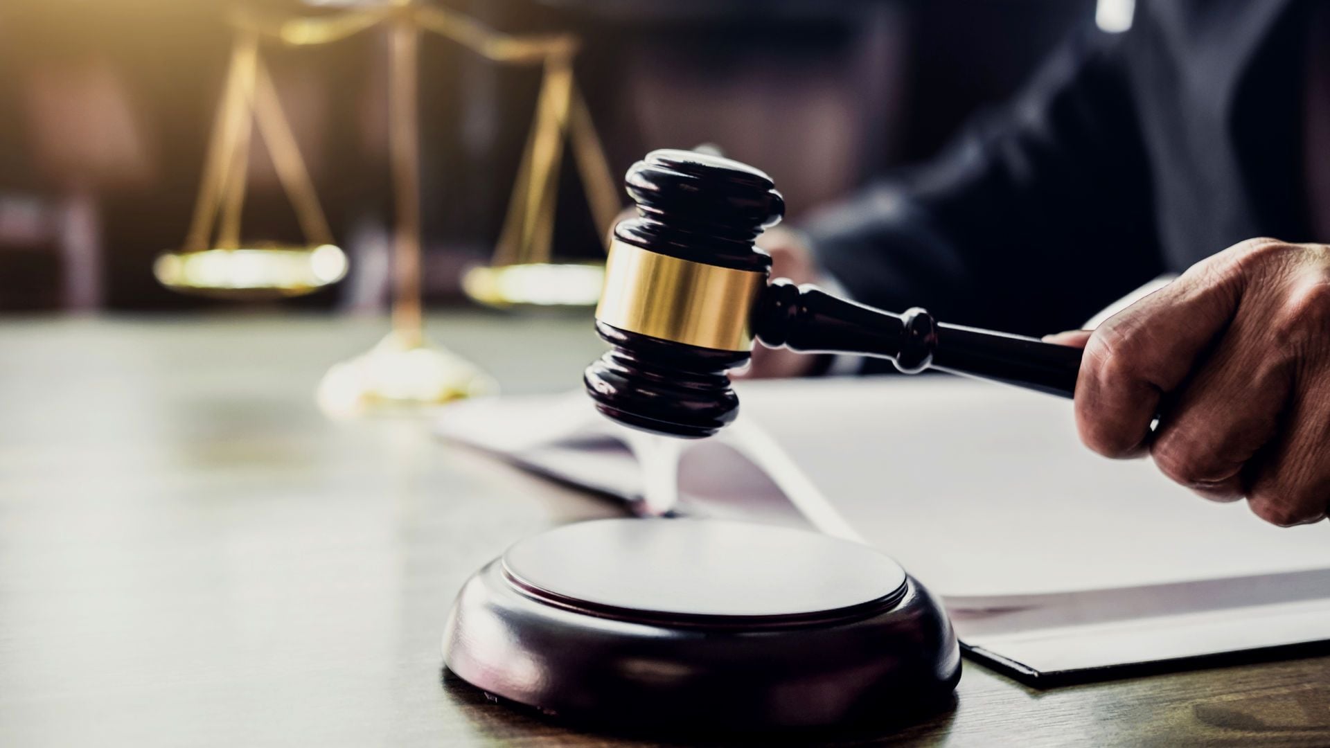 10. Cuándo Jesús deja de perdonar. A judge in a black robe about to use a gavel, with a digital tablet and a document on the table in front of them. Scales of justice are visible in the softly lit background. Opens a video in a new window.
