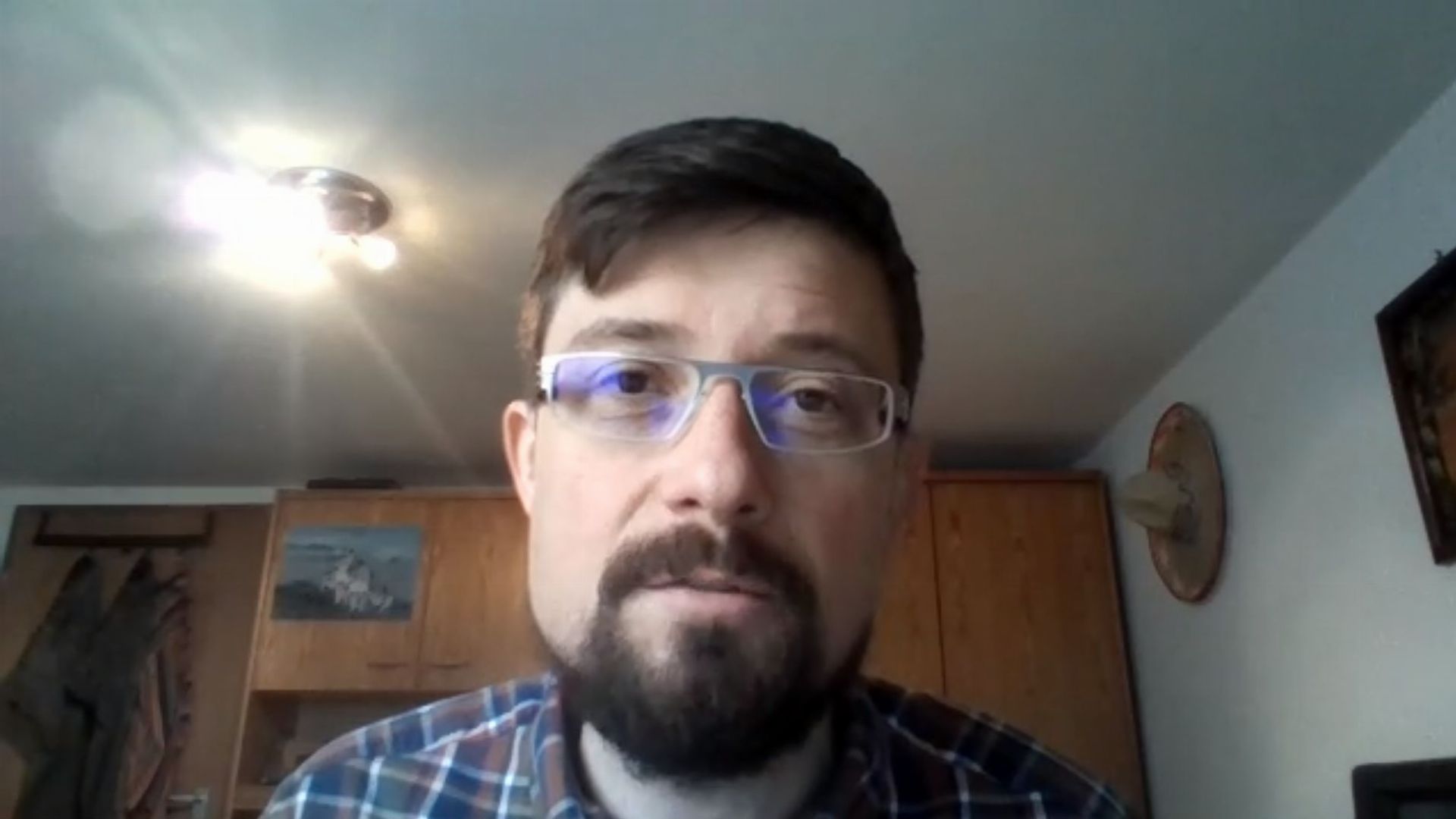 22. Das Gleichnis vom verlorenen Sohn - Lukasevangelium Kapitel 15. A man with a light beard and glasses sits in an indoor setting, with a wooden cabinet and a small framed artwork of a lake behind him. A ceiling light shines brightly above him. Opens a video in a new window.