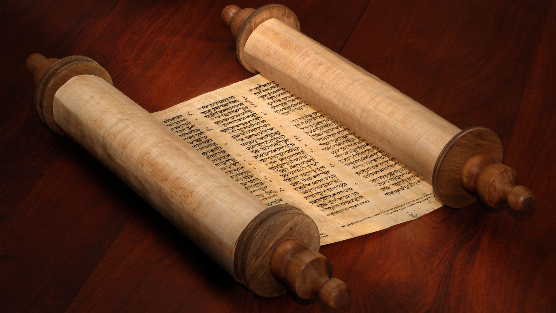 12. Gott verkündet das Ende von Anfang an. An ancient scroll open on a wooden table, with Hebrew text visible, possibly a sacred document. Opens a video in a new window.