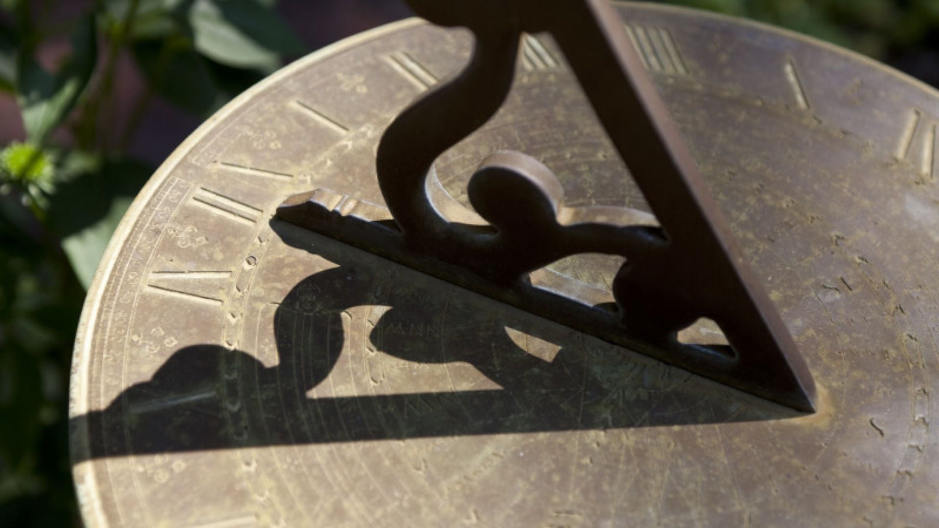 11. Die Hand Gottes auf der Sonnenuhr des Ahas. Close-up of a sundial with a triangular gnomon casting a shadow on a brass plate, which is intricately engraved with symbols associated with the Mazzaroth. Opens a video in a new window.
