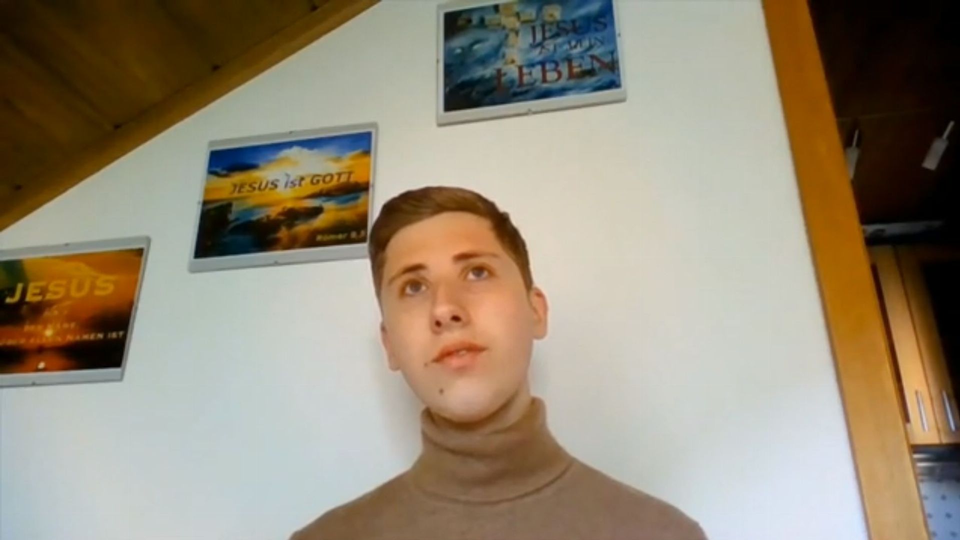 14. Die Wahrheit lässt sich finden!. A young man wearing a turtleneck looks upwards, expressing contemplation, in a room with religious-themed posters including celestial imagery and texts on the wall. Opens a video in a new window.