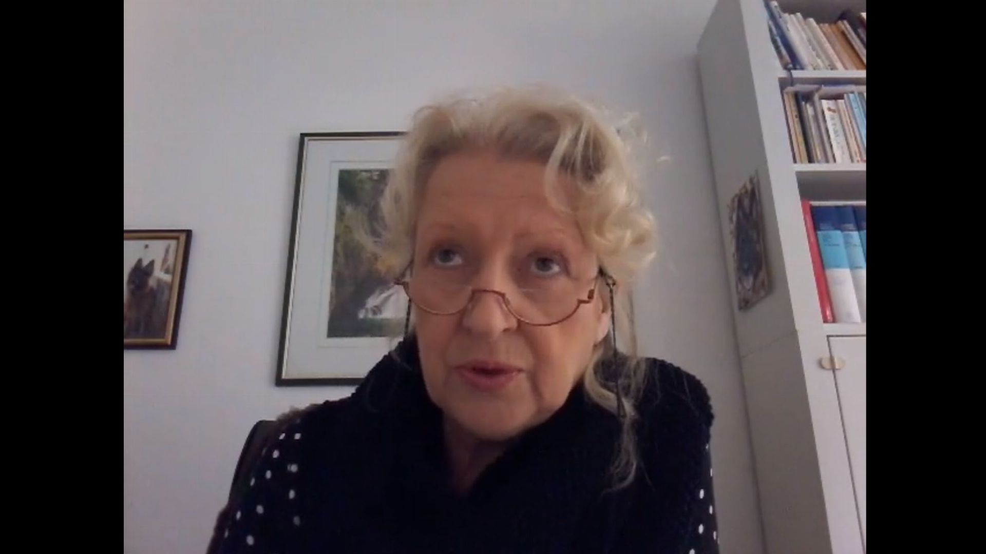 20. Wundersame Veränderungen sind mit Jesus immer möglich. An elderly woman with curly blonde hair wearing glasses and a black sweater adorned with dots. She appears to be engaging in a video call, with a room showing bookshelves and framed pictures in the background. Opens a video in a new window.