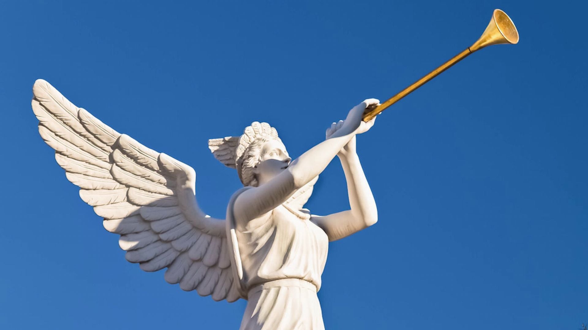 5. When Michael Stands Up. A white marble sculpture of an angel with extended wings, blowing a long trumpet against a clear blue sky. Opens a video in a new window.