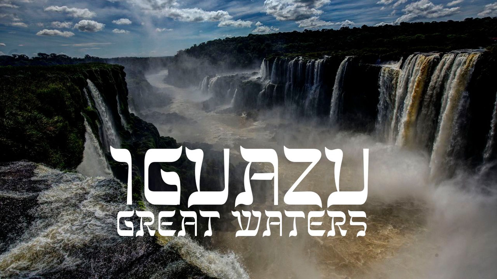 22. Iguazu - Great Waters. Majestic view of Iguazu Falls, showcasing cascading waterfalls plunging powerfully into mist-covered depths under a partly cloudy sky. Bold text overlay reads "IGUAZU GREAT WATERS". Opens a video in a new window.