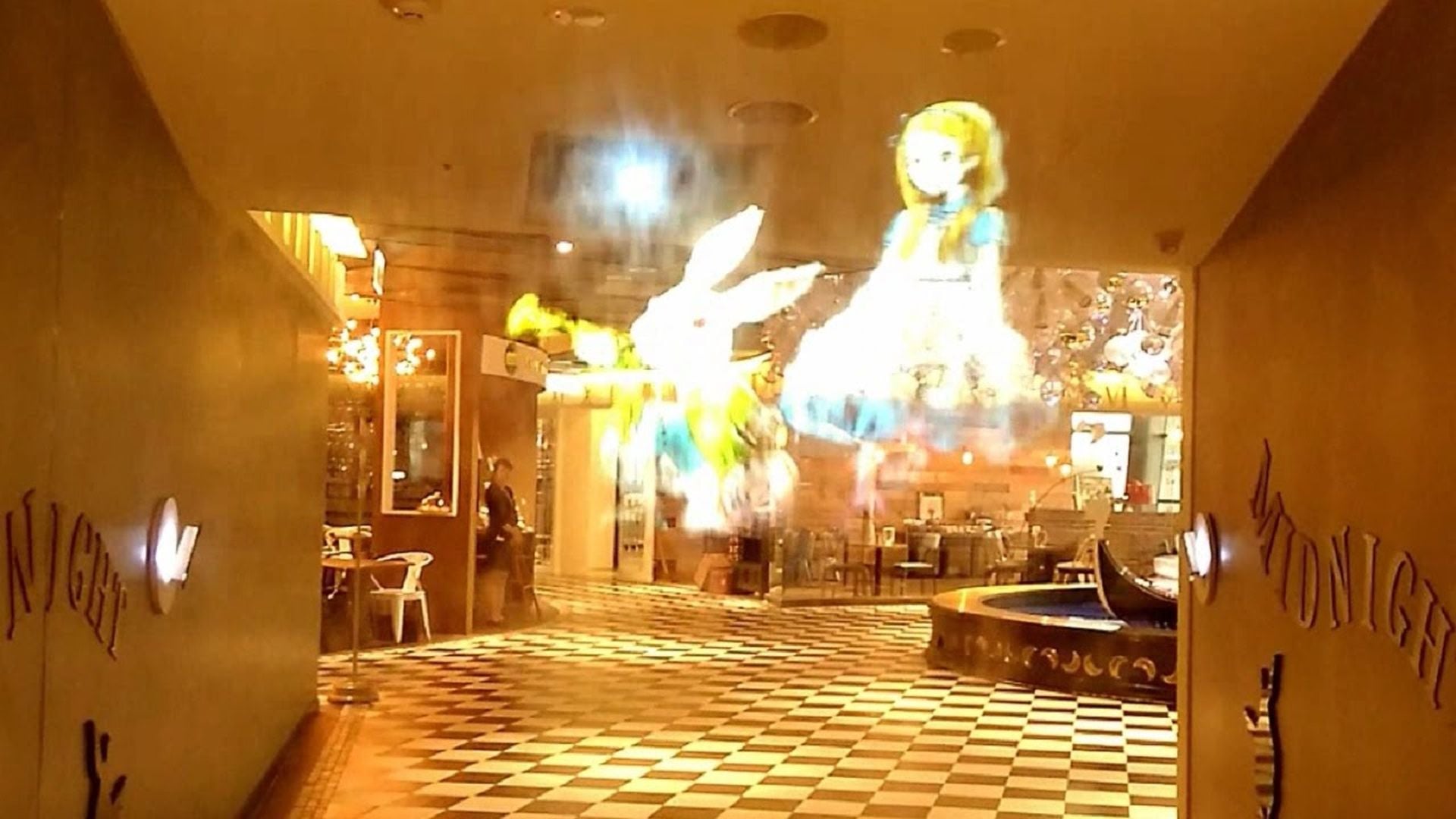 5. Großer holografischer Projektor - ein echter Anwendungsfall. Interior of a brightly lit venue with a checkered floor and holographic projection of a girl and a rabbit on the wall. A faint glow resembling celestial constellations illuminates the space, contributing to a mystical atmosphere reminiscent of the Mazzaroth. Opens a video in a new window.